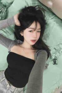KL Escort Girl Asian woman with black hair lying on a green pillow, wearing a black tube top and gray cardigan. Malaysia Sex Call Girl