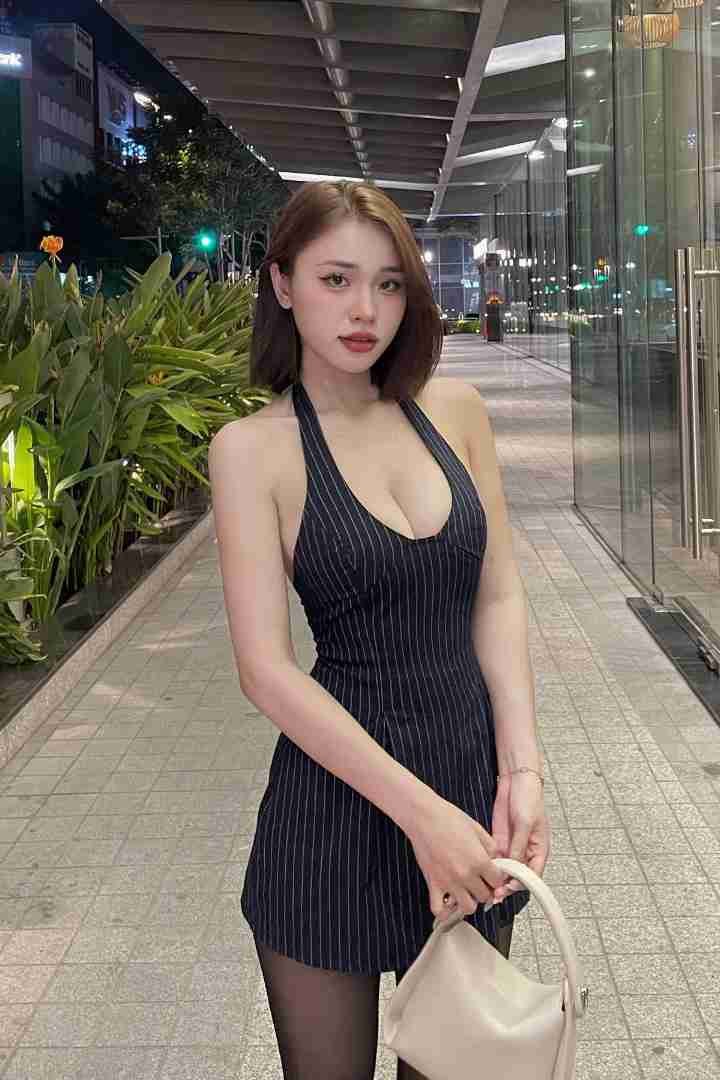 KL Escort Girl Stylish Asian woman in a pinstripe dress holding a white purse on a city street. Malaysia Sex Call Girl