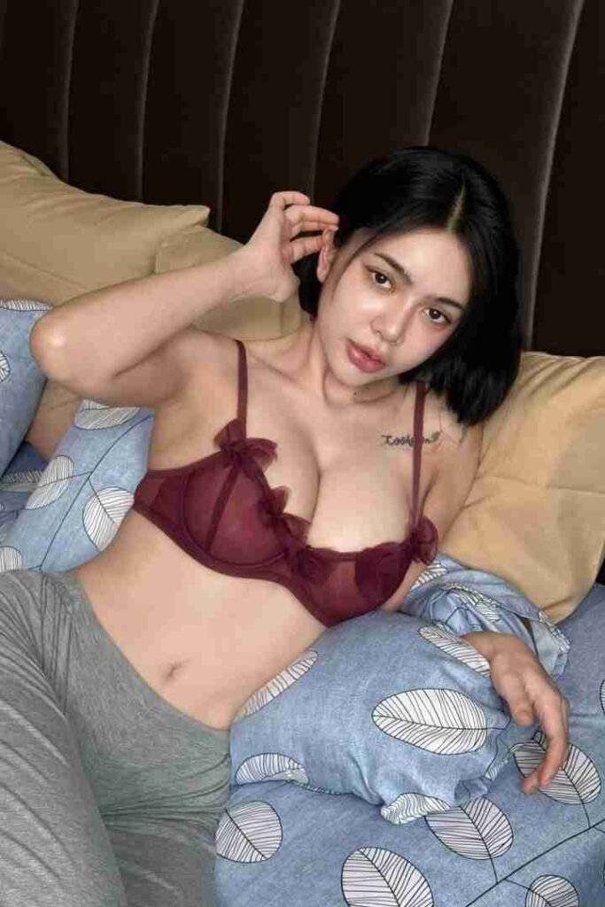KL Escort Girl Woman in lingerie lounging in bed on patterned sheets. Malaysia Sex Call Girl