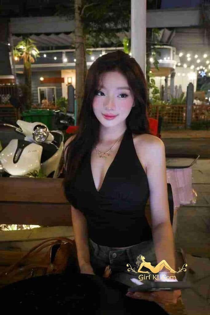 Attractive Asian woman with black halter top and phone outdoors at night.