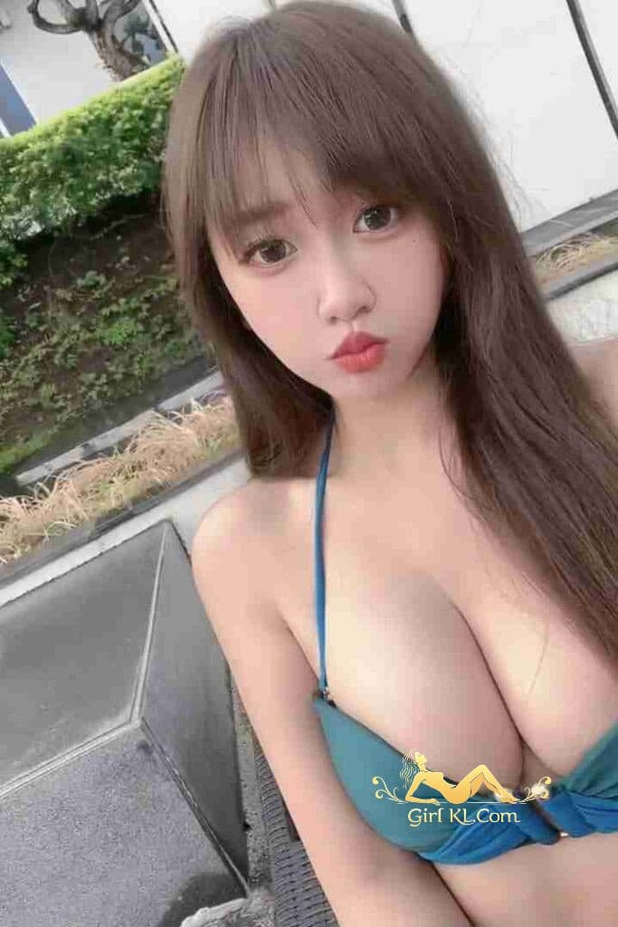 Attractive Asian woman in blue bikini top with long brown hair and bangs, pouting lips.