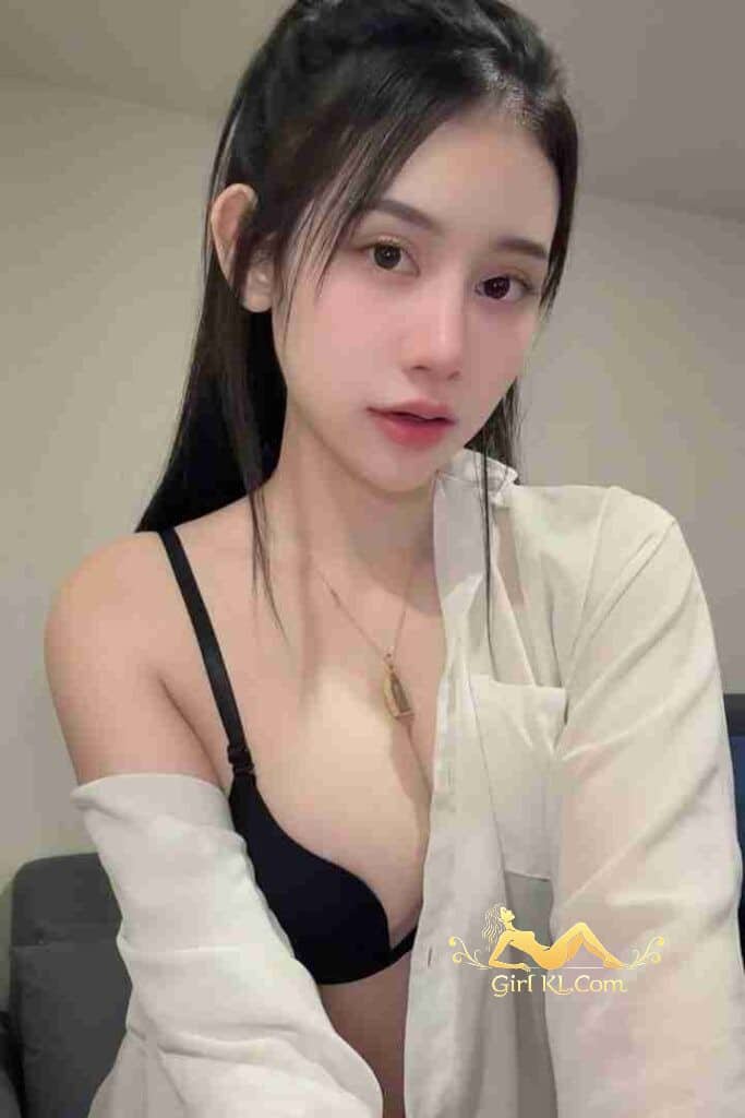 Attractive Asian woman in unbuttoned shirt and bra, posing indoors with necklace.