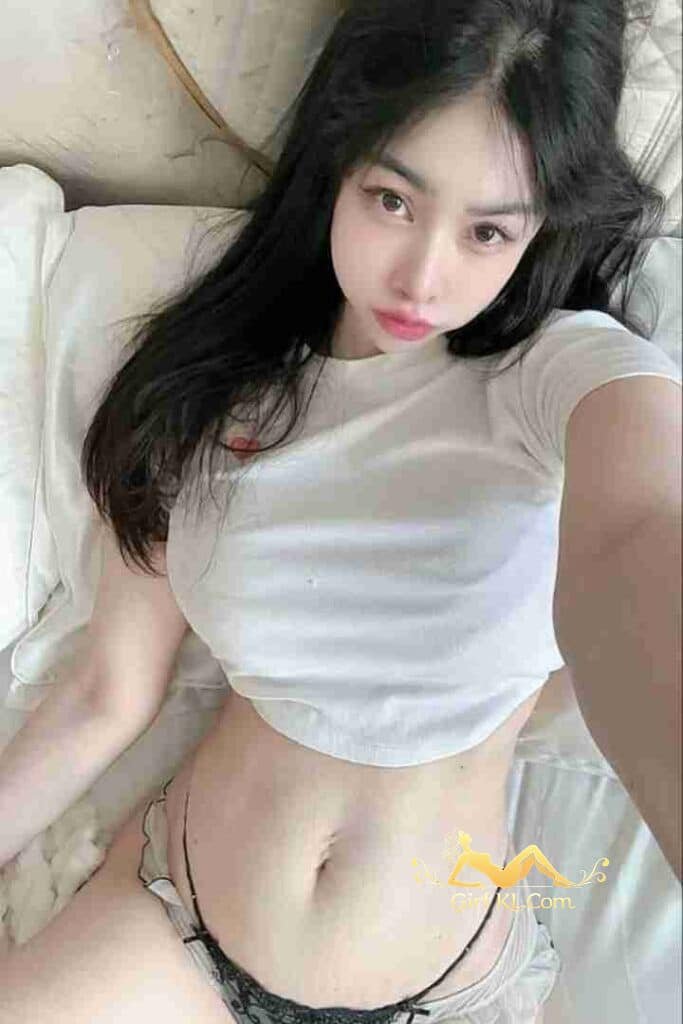 Beautiful Asian woman in crop top lying on bed. Black hair, light skin, pink lips. KL Escort Incall/Outcall Services.