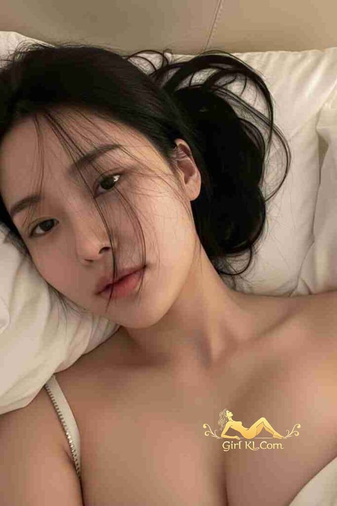 Attractive Asian woman with dark hair lying on a white pillow. VIP KL Escort.