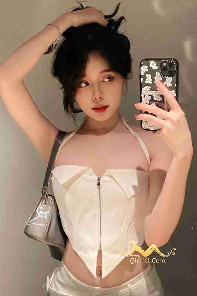 Attractive Asian woman in white corset top taking a selfie with phone.