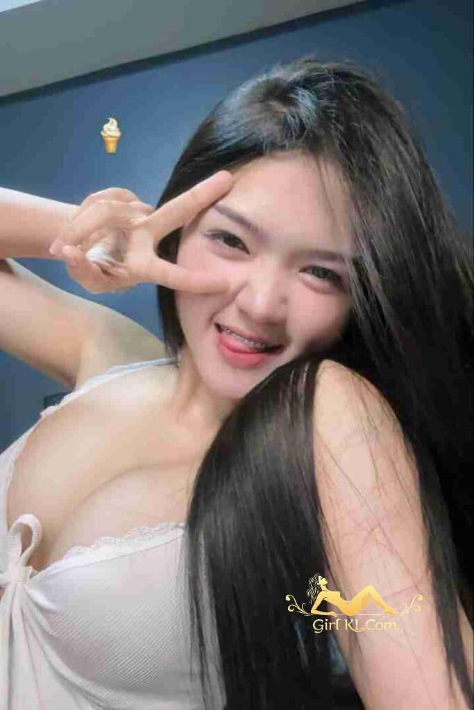 Attractive Thai woman, Kiera, with long black hair and braces, making a peace sign. B cup, 49kg, 164cm.