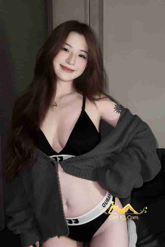 Petite Asian woman in black lingerie and gray sweater, smiling. Kuala Lumpur escort.