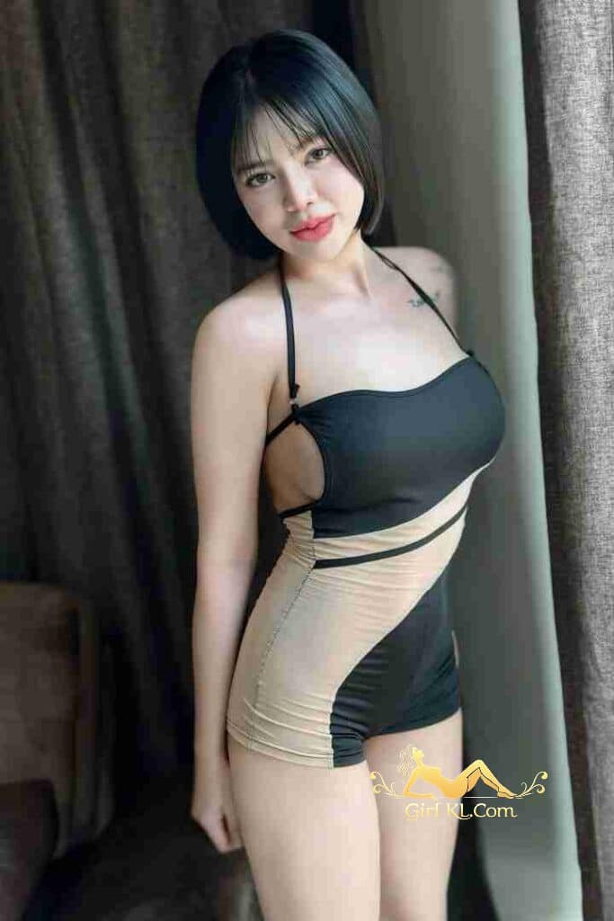 Thai babe in a black and beige swimsuit posing near curtains. KL Escort Risa.