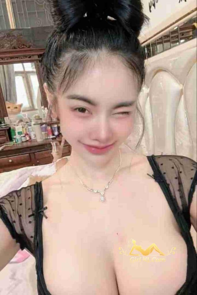 Thai woman winking, black top, bun hairstyle, necklace. D Cup, 48kg, 162cm.