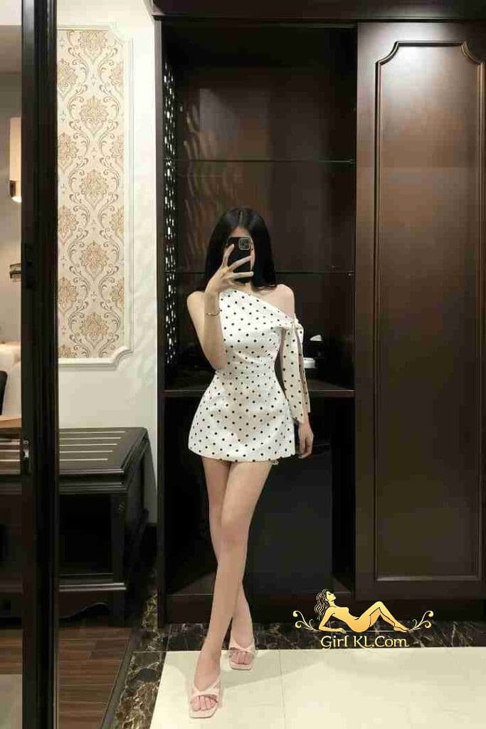 Vietnamese woman in polka dot dress, holding phone. Kuala Lumpur escort.