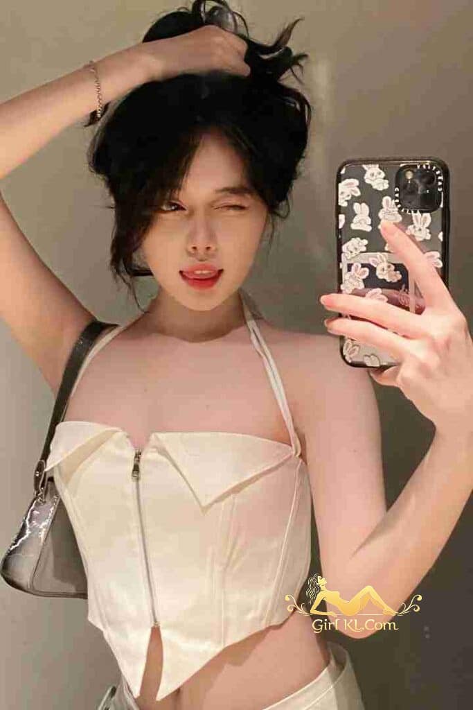 Winking Vietnamese woman in white corset top taking selfie.