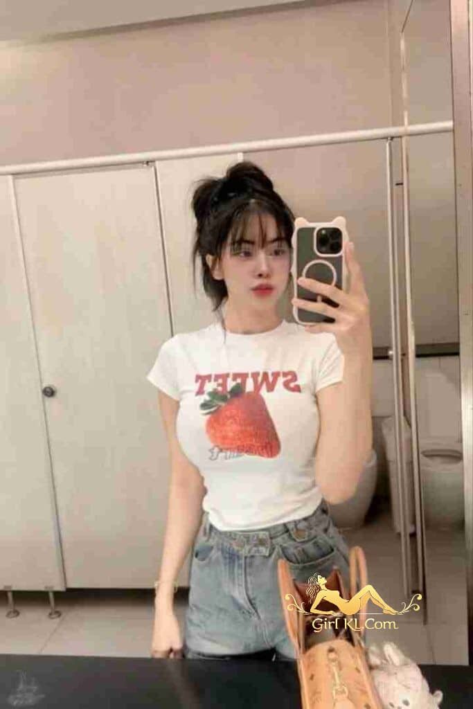Pretty woman in bathroom mirror selfie, wearing "Sweet" strawberry shirt.