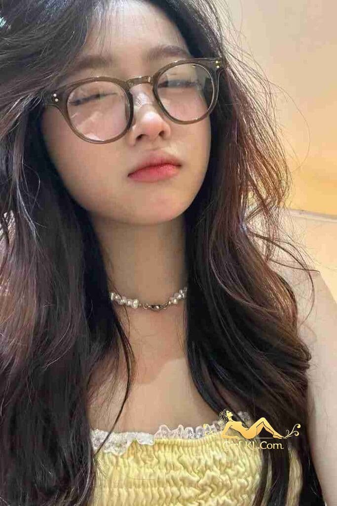 Attractive young Asian woman with glasses and pearl necklace in yellow top.